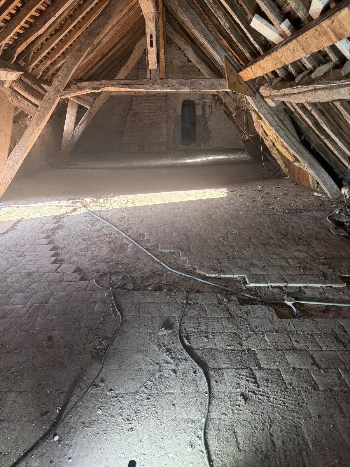 Grenier vidé avec sol en briques et charpente en bois apparente après débarras